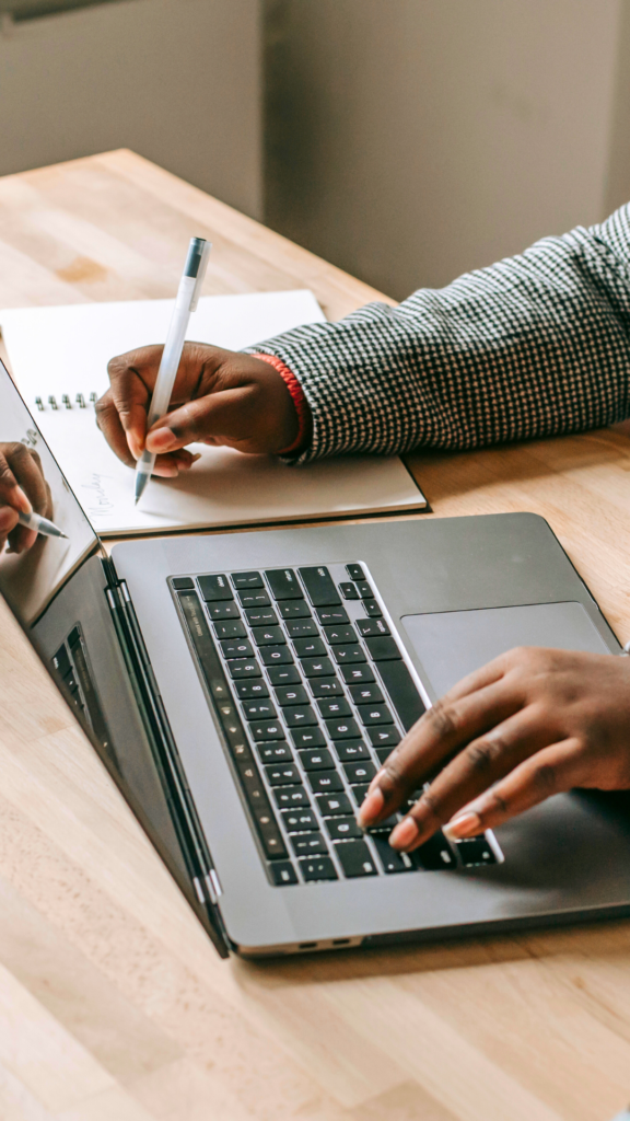 Black women's hands writing on notepad and typing on laptop