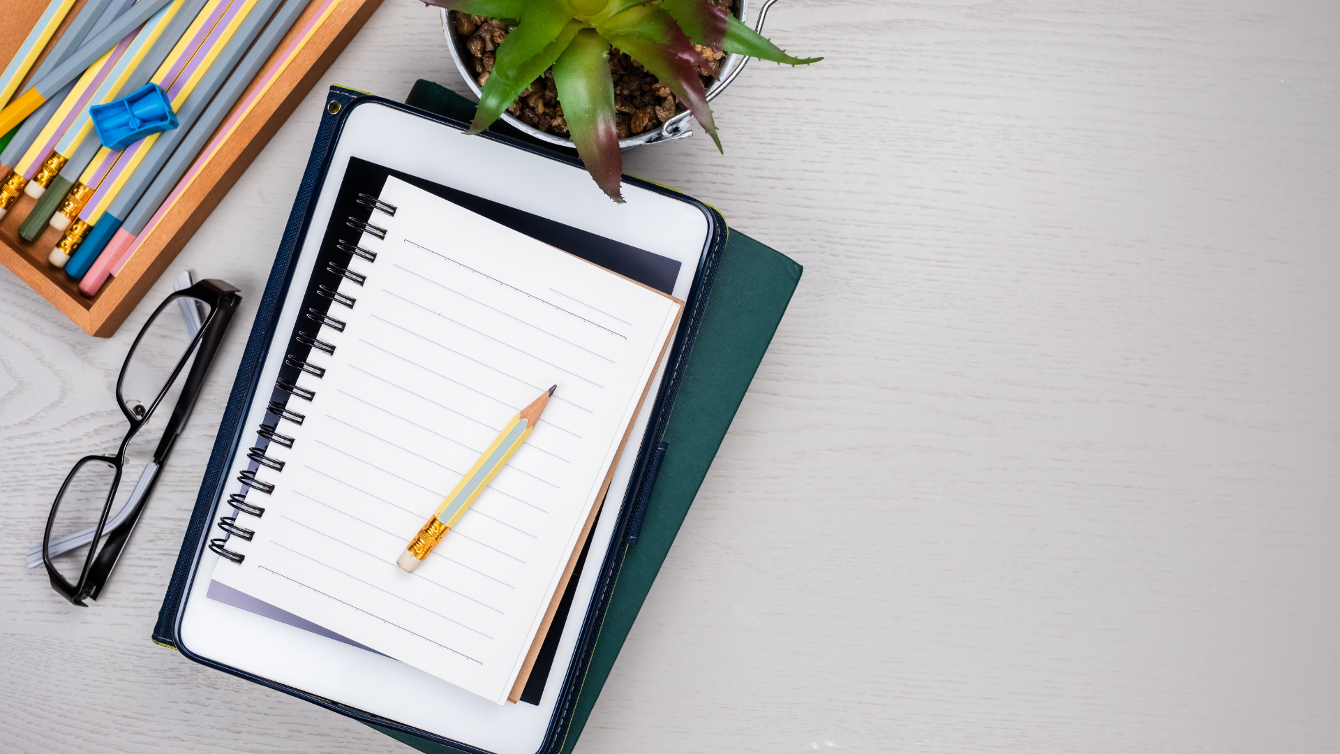 blank notebook laying on top of tablet next to set of pencils