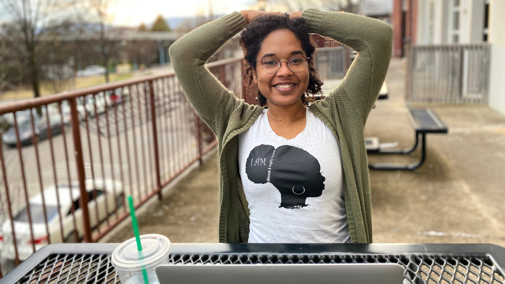 Smiling Shana stretching her arms above her head. wearing shirt with a black lady with curly ponytail